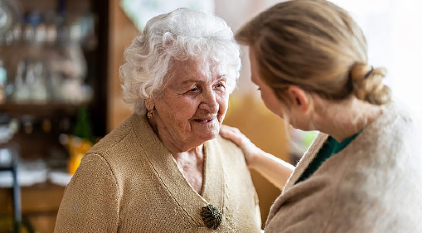 A carer sitting close to an older woman with a hand on her shoulder