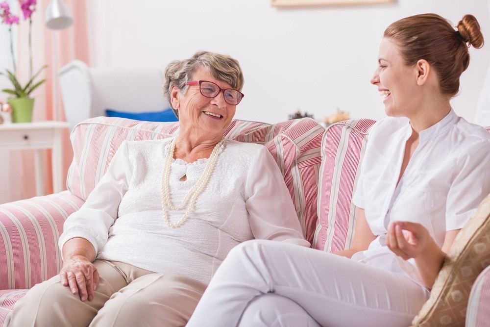 A live-in carer helping an elderly woman stand up at home
